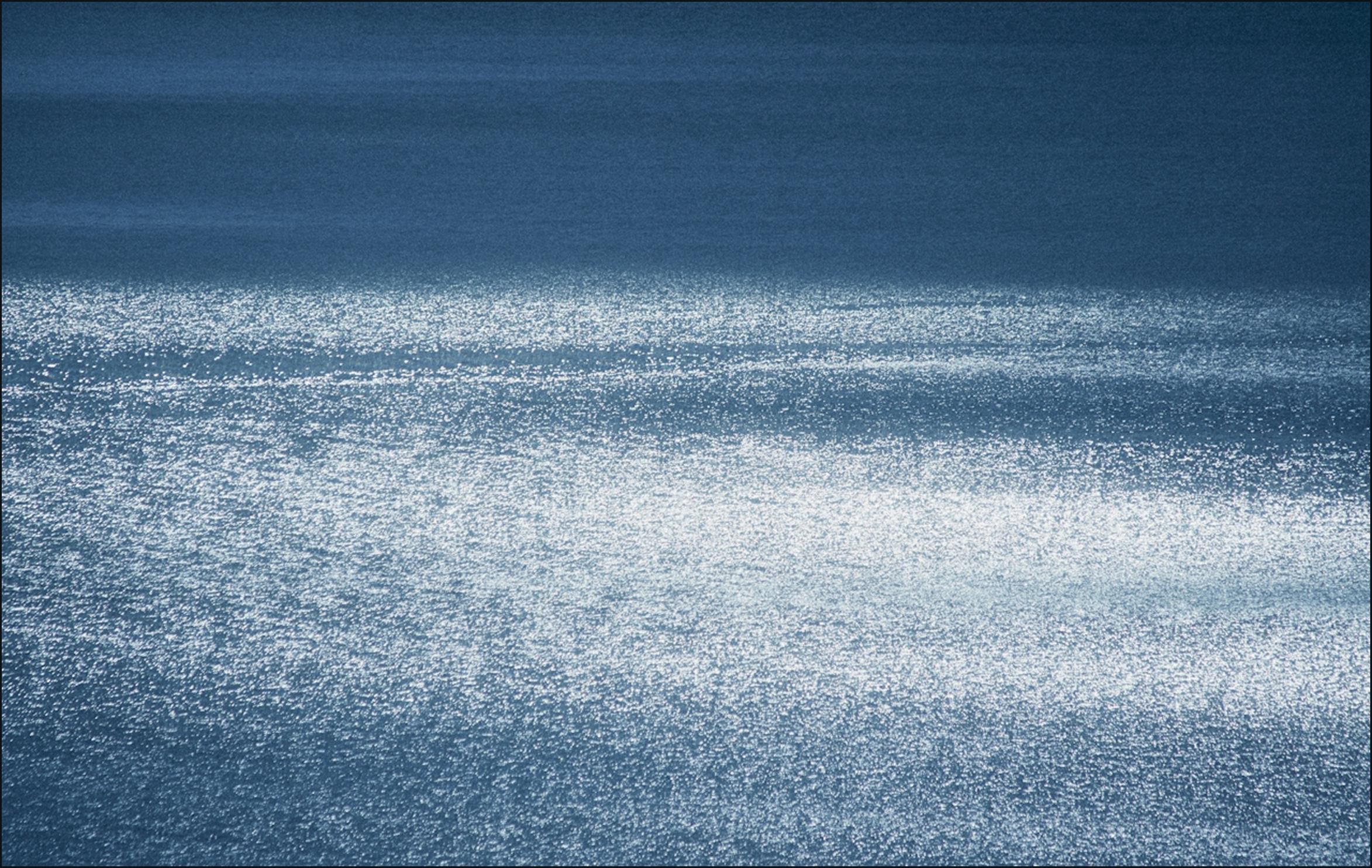 Sunlight glittering across a calm, deep blue open sea
